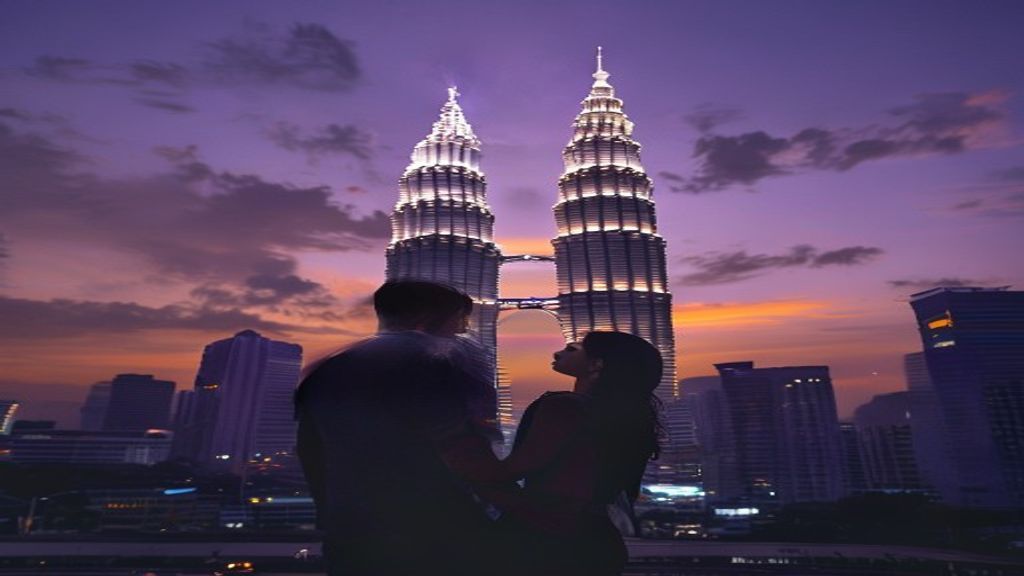 Young Indian couple standing in front of the Petronas Twin Towers in Kuala Lumpur at dusk